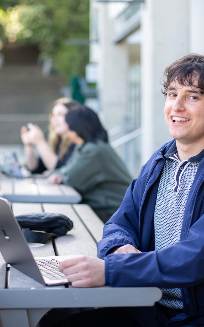 Smiling young man with a laptop sitting outside